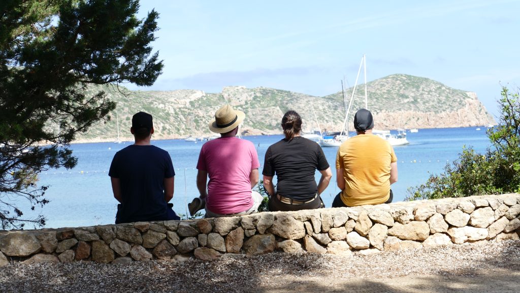 Vier Jungs auf einer Mauer schauen in die Bucht von Cabrera
